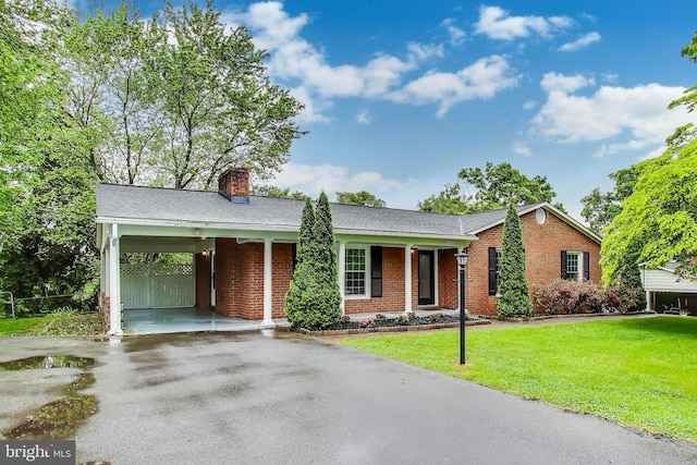 ranch-style home featuring brick siding, asphalt driveway, a chimney, a front yard, and an attached carport