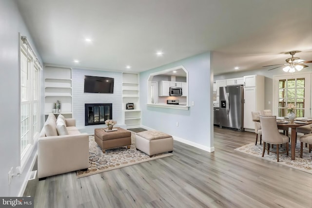 living room featuring wood finished floors, baseboards, recessed lighting, ceiling fan, and a fireplace