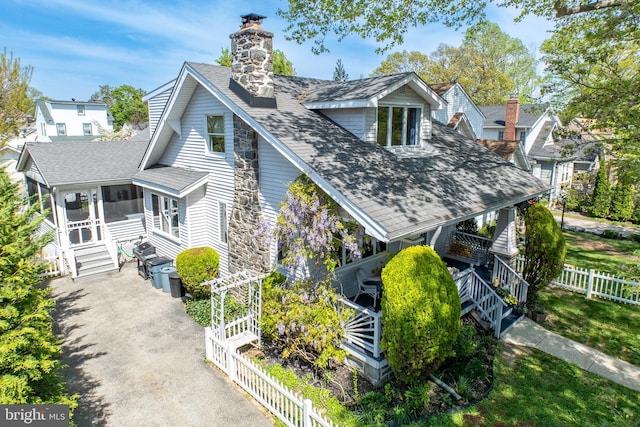 view of side of property featuring a chimney, fence, a sunroom, entry steps, and roof with shingles