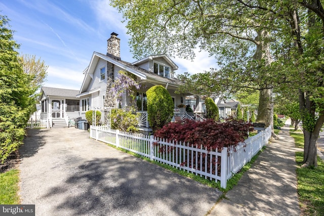view of front of property with a porch, a fenced front yard, asphalt driveway, a chimney, and a sunroom