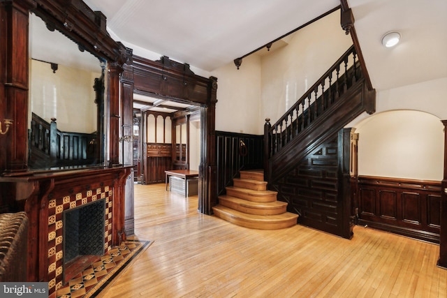 foyer featuring stairs, light wood-style floors, a fireplace, and a wainscoted wall