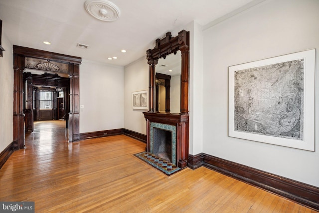 unfurnished living room featuring light wood finished floors, ornamental molding, baseboards, a high end fireplace, and recessed lighting