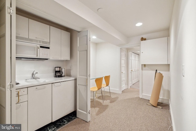 kitchen featuring a sink, white microwave, light countertops, light carpet, and recessed lighting