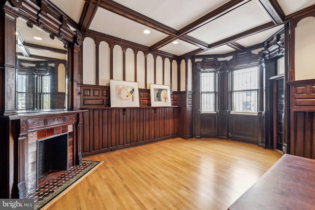 unfurnished living room with coffered ceiling, light wood-style floors, a decorative wall, beamed ceiling, and a fireplace