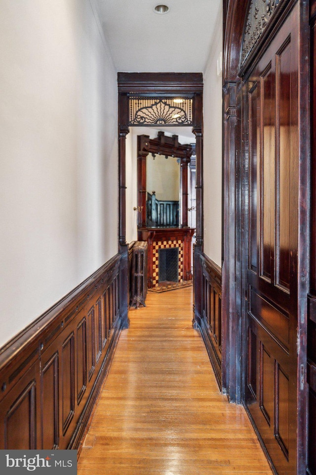 corridor with crown molding, a wainscoted wall, and light wood-type flooring