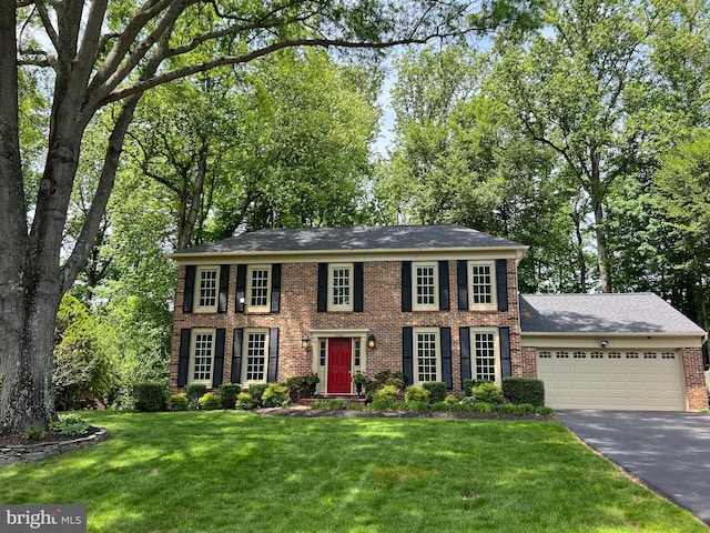 view of front of home with brick siding, asphalt driveway, an attached garage, and a front yard