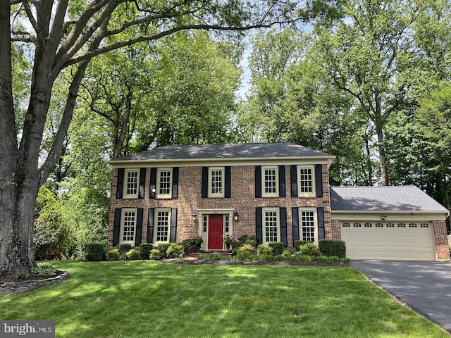 colonial inspired home featuring brick siding, asphalt driveway, a garage, and a front yard