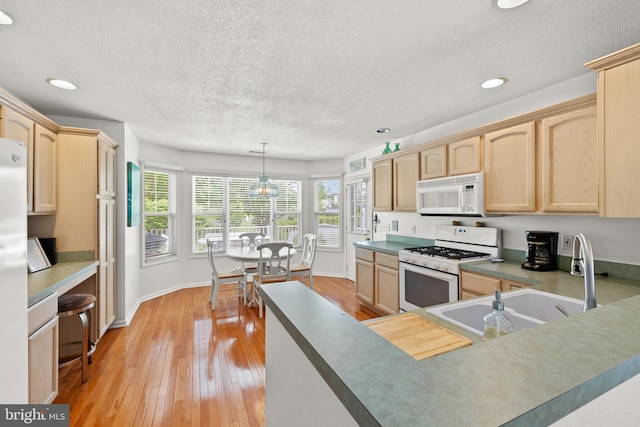 kitchen with white appliances, light brown cabinetry, a sink, a textured ceiling, and baseboards