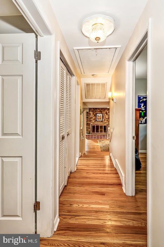 hallway with attic access, light wood-style flooring, and baseboards