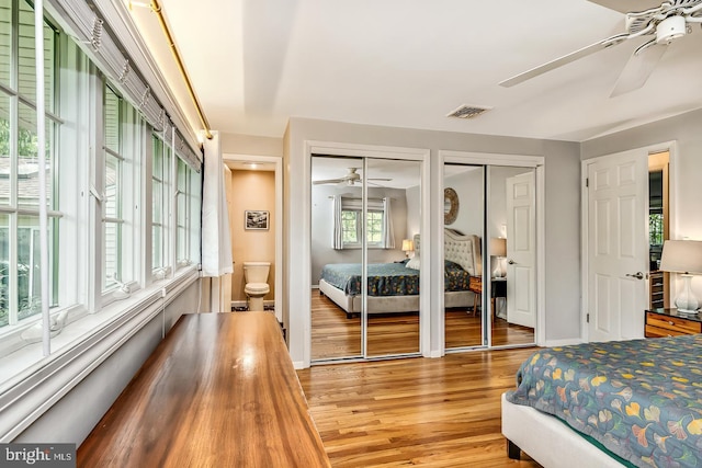 bedroom featuring two closets, light wood-type flooring, baseboards, ceiling fan, and ensuite bathroom