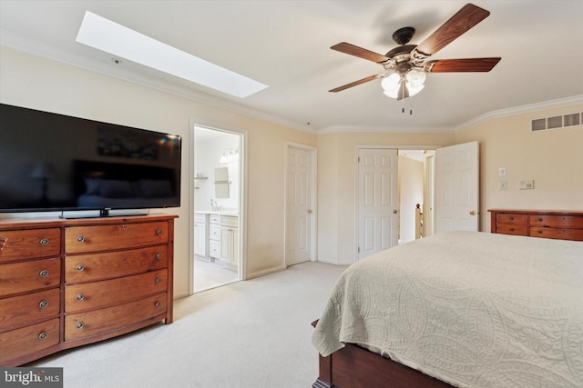 bedroom featuring a skylight, crown molding, light colored carpet, ensuite bath, and a ceiling fan