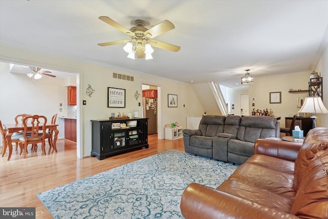 living area featuring ceiling fan, light wood finished floors, a chandelier, ornamental molding, and stairway