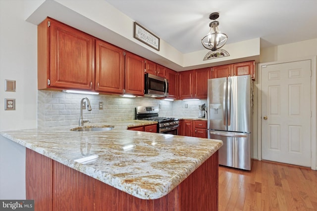 kitchen with stainless steel appliances, a sink, a peninsula, light stone countertops, and tasteful backsplash
