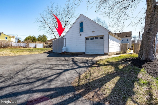 view of property exterior with driveway, fence, an outbuilding, and a garage