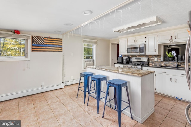 kitchen featuring appliances with stainless steel finishes, a sink, a kitchen island, light tile patterned flooring, and ornamental molding
