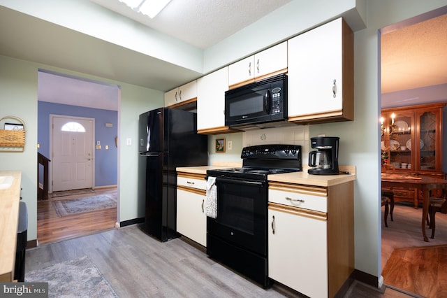 kitchen featuring black appliances, light countertops, light wood finished floors, and white cabinetry