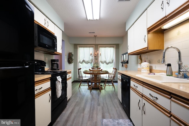 kitchen featuring black appliances, a sink, white cabinetry, wood finished floors, and a chandelier