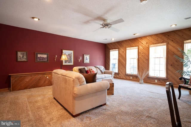 living room with carpet flooring, a textured ceiling, a ceiling fan, wood walls, and baseboards