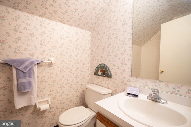 bathroom with wallpapered walls, vanity, toilet, and vaulted ceiling