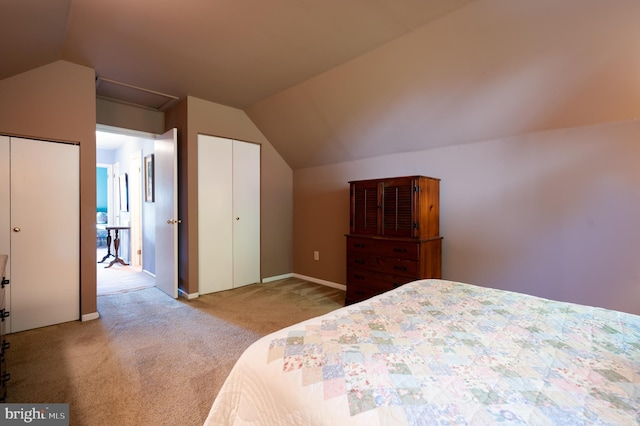 carpeted bedroom with vaulted ceiling, attic access, and two closets