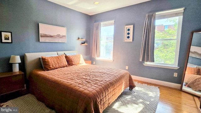 bedroom featuring wood finished floors, multiple windows, and baseboards