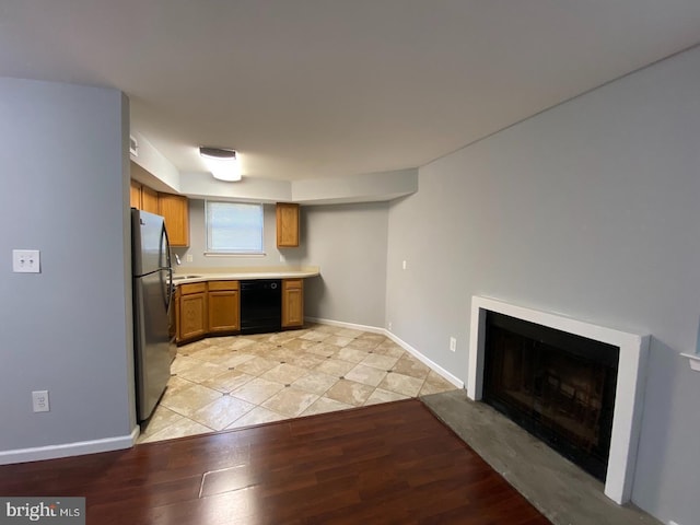 kitchen with freestanding refrigerator, black dishwasher, light wood-style flooring, light countertops, and a fireplace with raised hearth