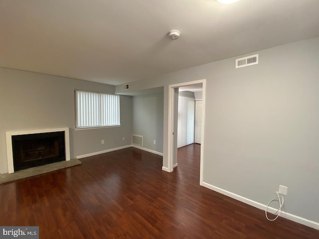 unfurnished living room with baseboards, dark wood-type flooring, and a fireplace with raised hearth