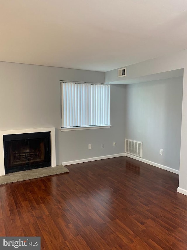 unfurnished living room with a fireplace with raised hearth, wood finished floors, and baseboards