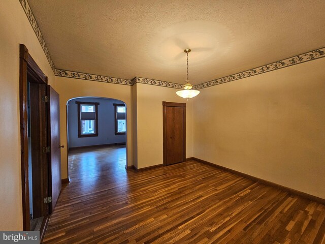 304 Pulaski St, Cumberland, MD 21502 - empty room featuring arched walkways, dark wood-style flooring, a textured ceiling, and baseboards