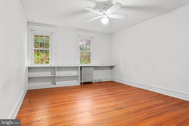 empty room with radiator, healthy amount of natural light, wood finished floors, and ceiling fan