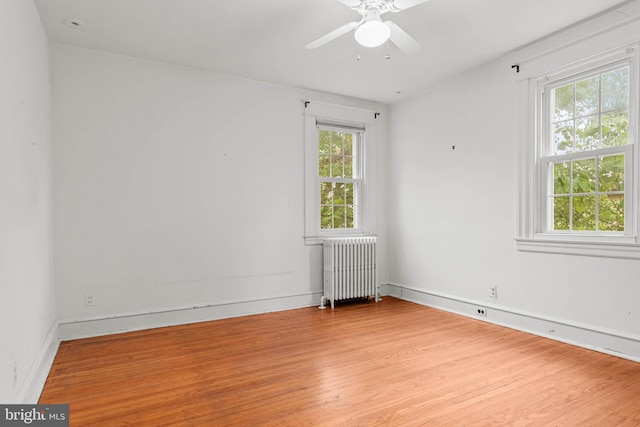 unfurnished room with radiator, wood finished floors, a ceiling fan, and baseboards