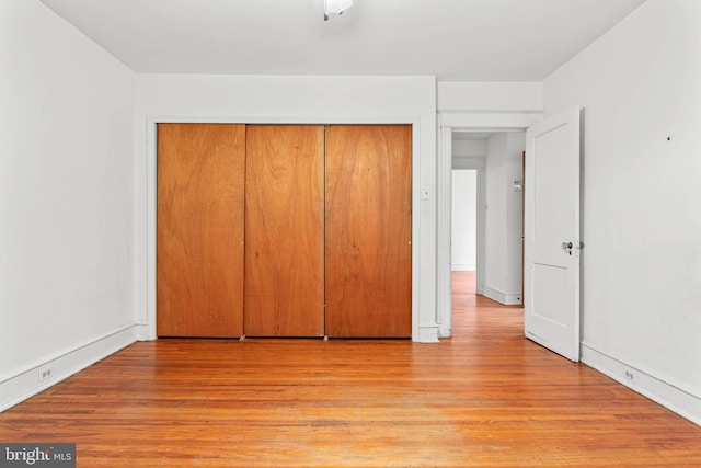 unfurnished bedroom featuring light wood finished floors, a closet, and baseboards