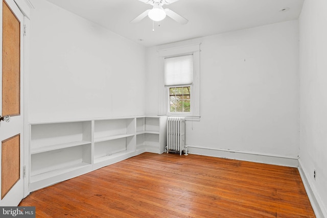 empty room featuring radiator heating unit, wood finished floors, a ceiling fan, and baseboards