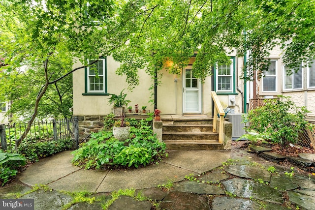 property entrance with central AC, stucco siding, and fence