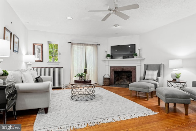 living room featuring radiator, wood finished floors, ceiling fan, a fireplace, and recessed lighting