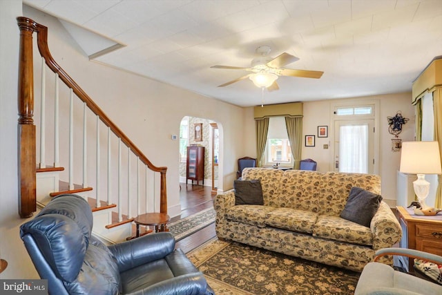 living room featuring arched walkways, ceiling fan, wood finished floors, and stairway