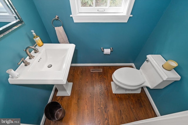 half bath featuring a sink, toilet, wood finished floors, and baseboards