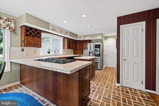 kitchen with stainless steel refrigerator with ice dispenser, gas stovetop, brick floors, plenty of natural light, and recessed lighting
