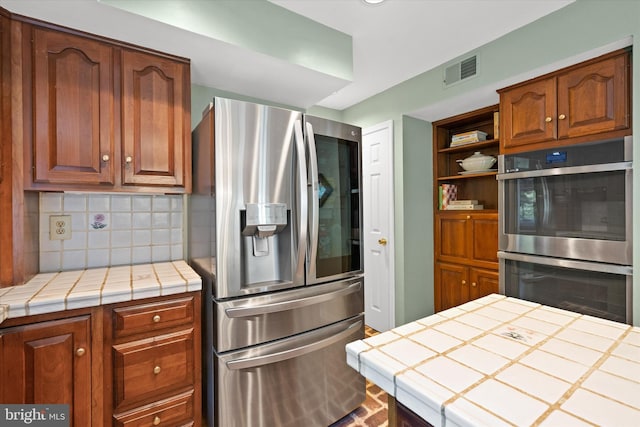 kitchen featuring appliances with stainless steel finishes, tile countertops, tasteful backsplash, open shelves, and brown cabinets