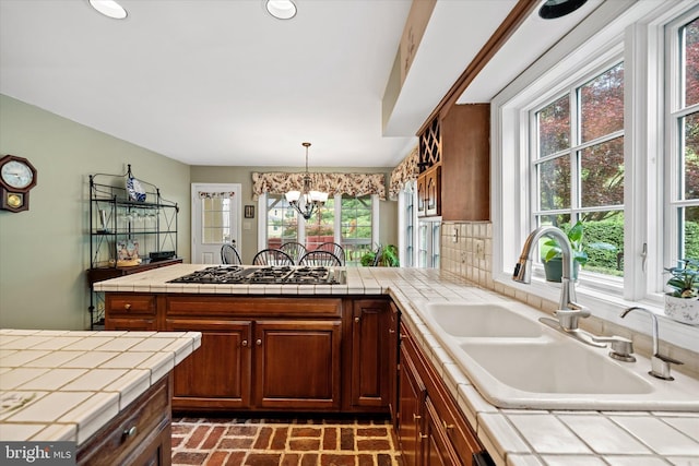 kitchen with tile countertops, a sink, brick patterned floors, gas stovetop, and a peninsula