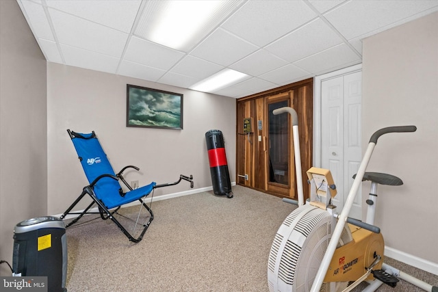 exercise area featuring baseboards, a paneled ceiling, and carpet