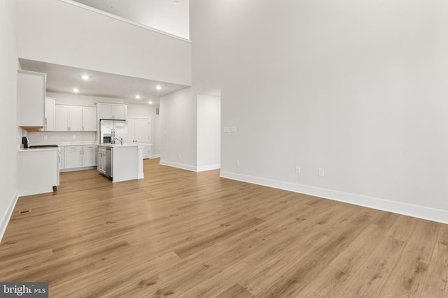 508 Waters Landing Dr, Essex, MD 21221 - unfurnished living room with baseboards, light wood-style flooring, recessed lighting, and a towering ceiling