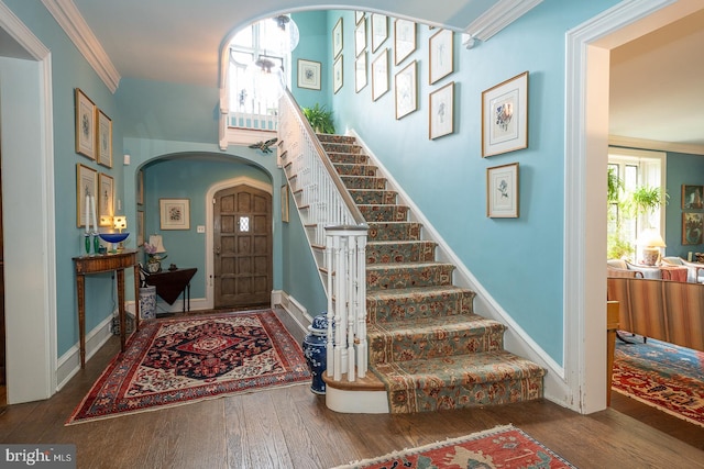 entryway featuring arched walkways, hardwood / wood-style floors, stairs, crown molding, and baseboards