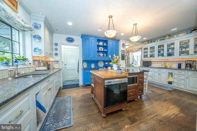 kitchen with a sink, black oven, stainless steel microwave, wood counters, and open shelves
