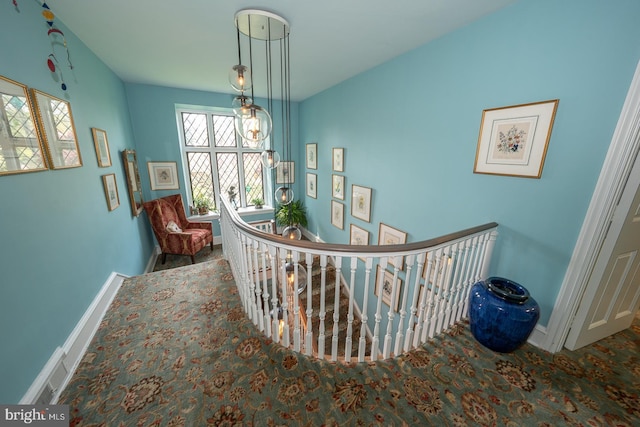 hallway with an upstairs landing, carpet, and baseboards