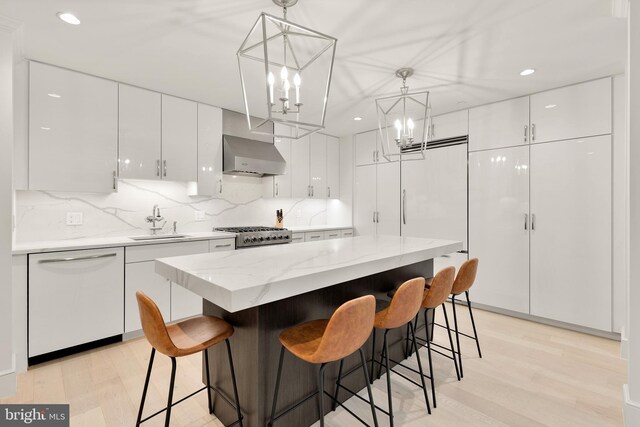 2122 N St NW Unit 1, Washington, DC 20037 - kitchen with white dishwasher, wall chimney range hood, a sink, light wood-style flooring, and white cabinets