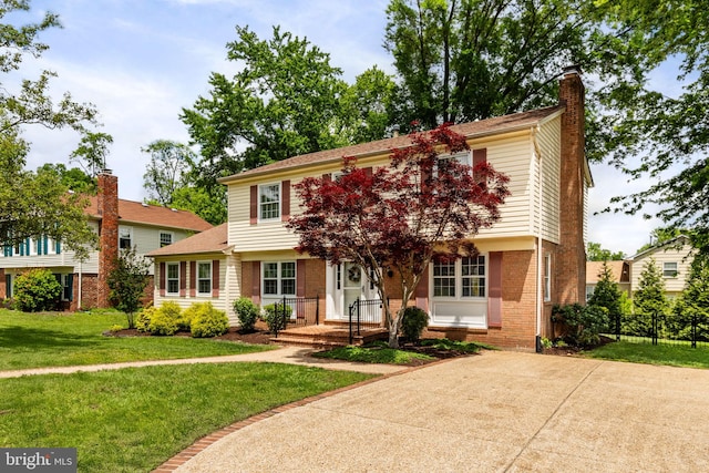 colonial inspired home with a chimney, a front lawn, and brick siding