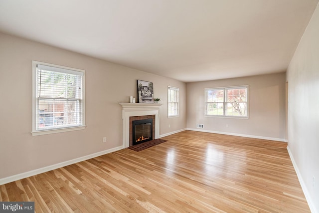 unfurnished living room with a fireplace with flush hearth, healthy amount of natural light, light wood-type flooring, and baseboards