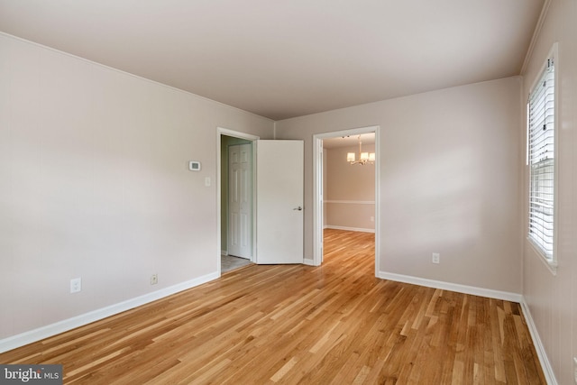 spare room featuring a chandelier, light wood finished floors, and baseboards