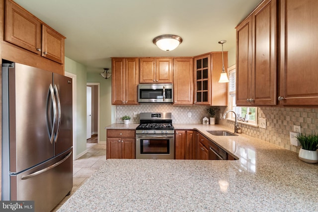 kitchen with appliances with stainless steel finishes, a sink, tasteful backsplash, light stone countertops, and glass insert cabinets